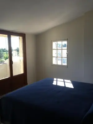 a bedroom with a blue bed and two windows at Ancienne Maison des Gardes in Lourmarin