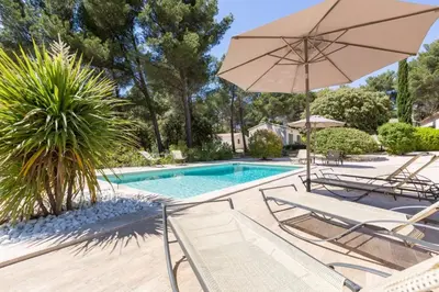 a swimming pool with chairs and an umbrella at Les Mazets du Luberon in Puget