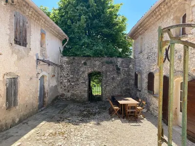a wooden table in the courtyard of a stone building at Provencal farmhouse in Luberon's heart with pool in La Bastide-des-Jourdans