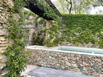 a stone wall with a swimming pool in front of a building at Mas de 190m2 Climatisé avec Piscine et Cuisine d'été - 10 pers in La Fare-les-Oliviers
