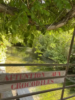 a sign on a fence with a river in the background at Studio Rdc proche Quai Rouget in LʼIsle-sur-la-Sorgue