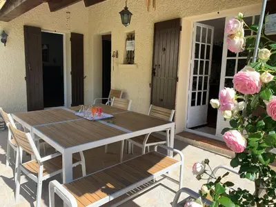 a wooden table and chairs on a patio with pink roses at Villa Marie-Rose in Saint-Didier