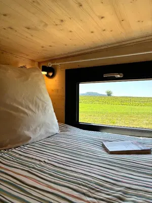 a bed in a room with a window with a book on it at La Tiny House des Vignes du Château de Vauclaire in Meyrargues