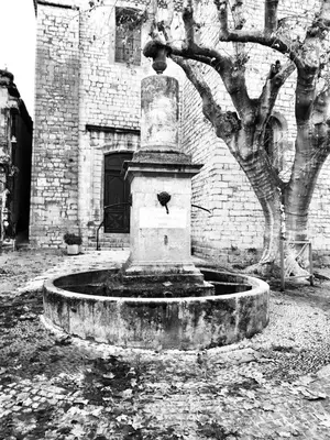 a fountain in front of a brick building with a tree at Charmante maison de village dans le Luberon in Beaumont-de-Pertuis