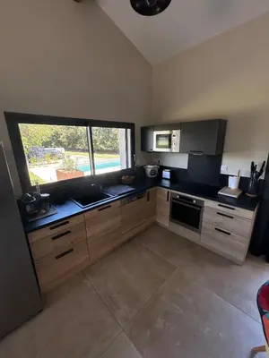 a kitchen with wooden cabinets and a large window at Charmante maison avec piscine et grand jardin in LʼIsle-sur-la-Sorgue
