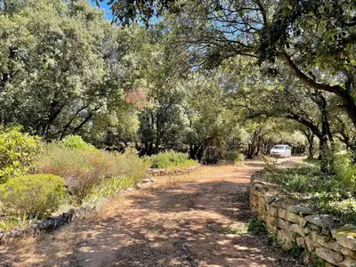 a dirt road with a stone wall and a car on it at Maison paisible au coeur du Luberon in Bonnieux