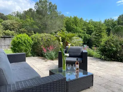 a patio with a couch and a table with a bottle of wine at Une maison en Provence piscine au pied du Luberon in Mérindol