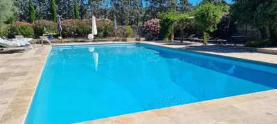 a blue swimming pool with chairs and trees at La BERGERIE in Pélissanne