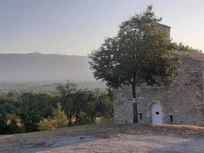 a building with a tree on top of a hill at Petit gîte et Grande piscine in Blauvac