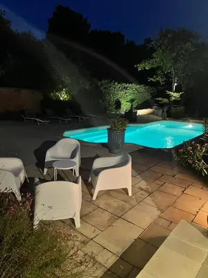 a group of chairs sitting next to a swimming pool at night at Le Bois De La Cour in Roussillon