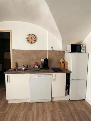 a kitchen with white cabinets and a clock on the wall at Cosy Cœur Alpilles, T2 neuf in Aureille