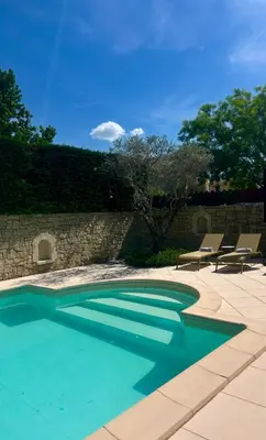 a swimming pool with two chairs and a stone wall at Chambre L in Les Taillades