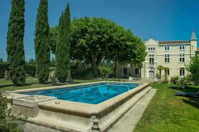 a swimming pool in front of a house with trees at Château vert in Cavaillon