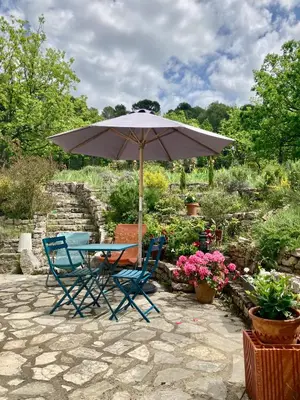 a table and chairs under an umbrella in a garden at Les oliviers in Saignon