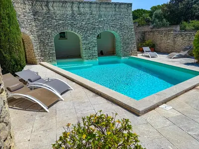 a swimming pool with two chairs and a stone wall at Villa de vacances à Gordes avec piscine partagée, La Bastide de Léa in Gordes