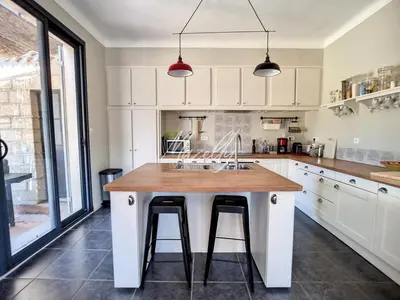 a kitchen with white cabinets and a wooden island with bar stools at La Villa Luberonnaise in Robion en Luberon