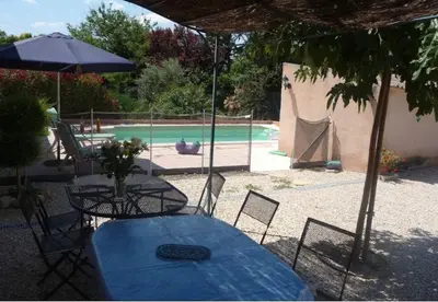 a table and chairs with an umbrella and a pool at Ferme au pied du luberon in Lourmarin