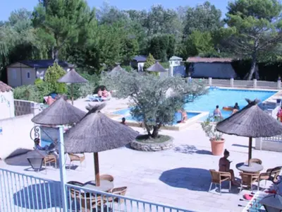 a swimming pool with umbrellas and people sitting around it at Chalet confort avec terrasse - 5 personnes - API-1-52-621 in Noves