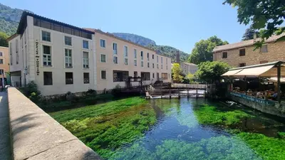 a river in the middle of a city with buildings at La Cour de Pétrarque in Fontaine-de-Vaucluse