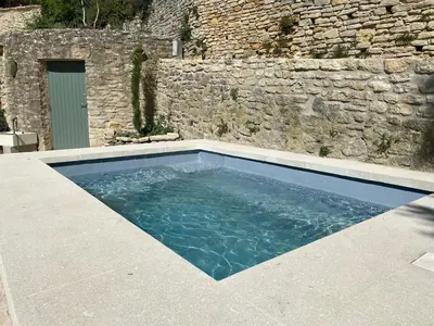 a swimming pool in front of a stone wall at Bastidon, Petite bastide pour 2 avec bassin et jardin privé in Crillon-le-Brave