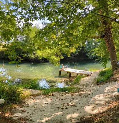 a person sitting on a bench next to a river at La Bergerie des Sorgues in LʼIsle-sur-la-Sorgue