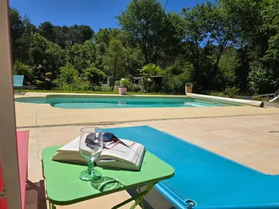 a table with a wine glass and a book next to a swimming pool at studio à la campagne avec piscine in Peyrolles-en-Provence