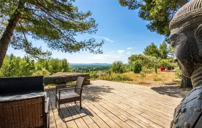 a wooden deck with two chairs and a statue at Maison Piscine Proche Alpilles in Noves