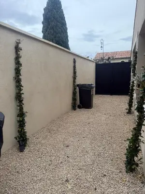 a fence with a trash can and two plants at Charmant appartement T2 cosy avec piscine in Mollégès