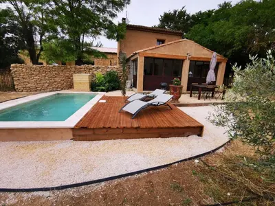 a pool with a wooden deck next to a house at Petit mas en Provence in Cornillon-Confoux