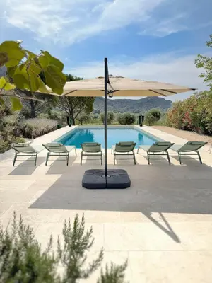 a tan umbrella and chairs next to a swimming pool at La Villa des Glauges in Eyguières
