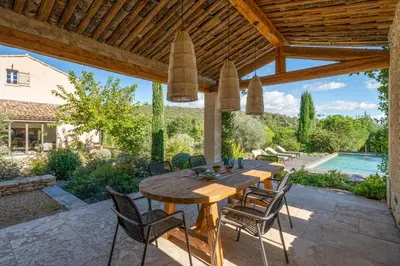a wooden table and chairs on a patio with a pool at Bastide de Guby in Saint-Saturnin-les-Apt