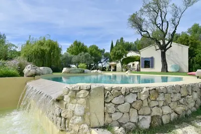 a swimming pool with a stone wall next to a house at Maison Satine in Noves