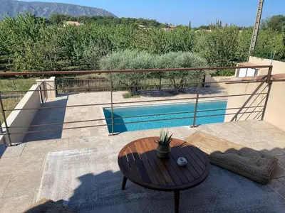 a wooden table sitting on a patio with a pool at Villa contemporaine avec piscine - 5 min de Gordes - vue sur le Luberon in Cabrières-dʼAvignon