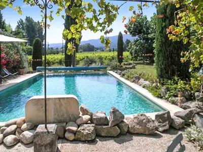 a pool with a chair and rocks in a yard at Maison charmante à Oppède avec vue sur la montagne in Oppède