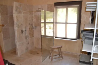 a shower with a glass door and a stool in a bathroom at Mas Ste Hélène in Céreste