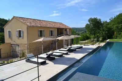 a pool with lounge chairs and umbrellas next to a house at Mas Ste Hélène in Céreste