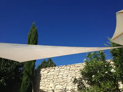 awning over a stone wall next to a tree at Le Petit Bastidon - Private pool - Gordes in Gordes
