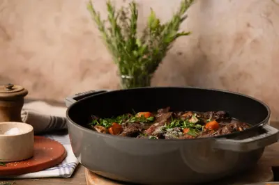 a pan of beef stew on a table with a vase of flowers at Campanile Prime - Aix-en-Provence Sud - Pont de l'Arc in Aix-en-Provence