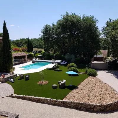 a backyard with a swimming pool and a lawn with chairs and an umbrella at Le Mas Vigneron in Gordes