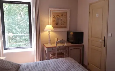 a bedroom with a bed and a desk with a television at Hotel du Poète in Fontaine-de-Vaucluse