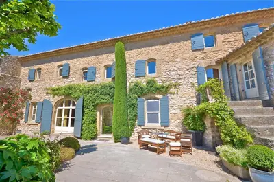a large stone building with blue shutters and a patio at Ferme St Roch in Robion en Luberon