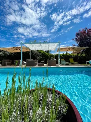 a swimming pool with blue water and umbrellas at La belle histoire Gîte Montmirail in Bédoin