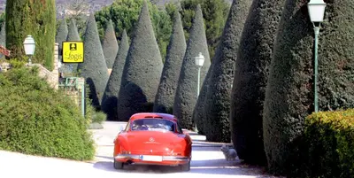 an old red car driving down a road with trees at Hôtel Carcarille Restaurant Le C in Gordes