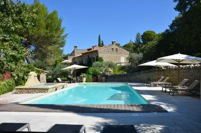 a swimming pool with chairs and umbrellas next to a house at Le Jas des Parpaillous in LʼIsle-sur-la-Sorgue