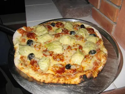 a pizza with olives and cheese on a pan at Ll POULIDETTO in Lioux