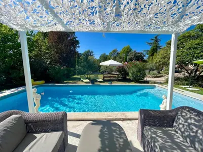 a swimming pool with two chairs and an umbrella at La belle histoire gîte Luberon in Bédoin