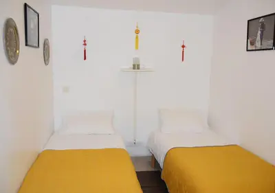 two beds in a room with white walls and yellow sheets at La Maison Des Invites in Pernes-les-Fontaines