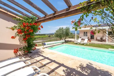 a pool with white chairs and red flowers next to a house at Les Terrasses de Cascavelle in Blauvac