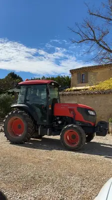 a red tractor parked in a gravel parking lot at Bastide Bellugue Maison d'hôtes réseau Bienvenue à La Ferme à 3 minutes de Lourmarin in Cadenet