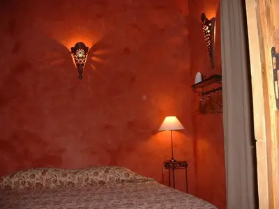 a bedroom with a red wall with a bed and a lamp at Gites Climatisés Piscine Chauffée La Balancelle in Saint-Rémy-de-Provence